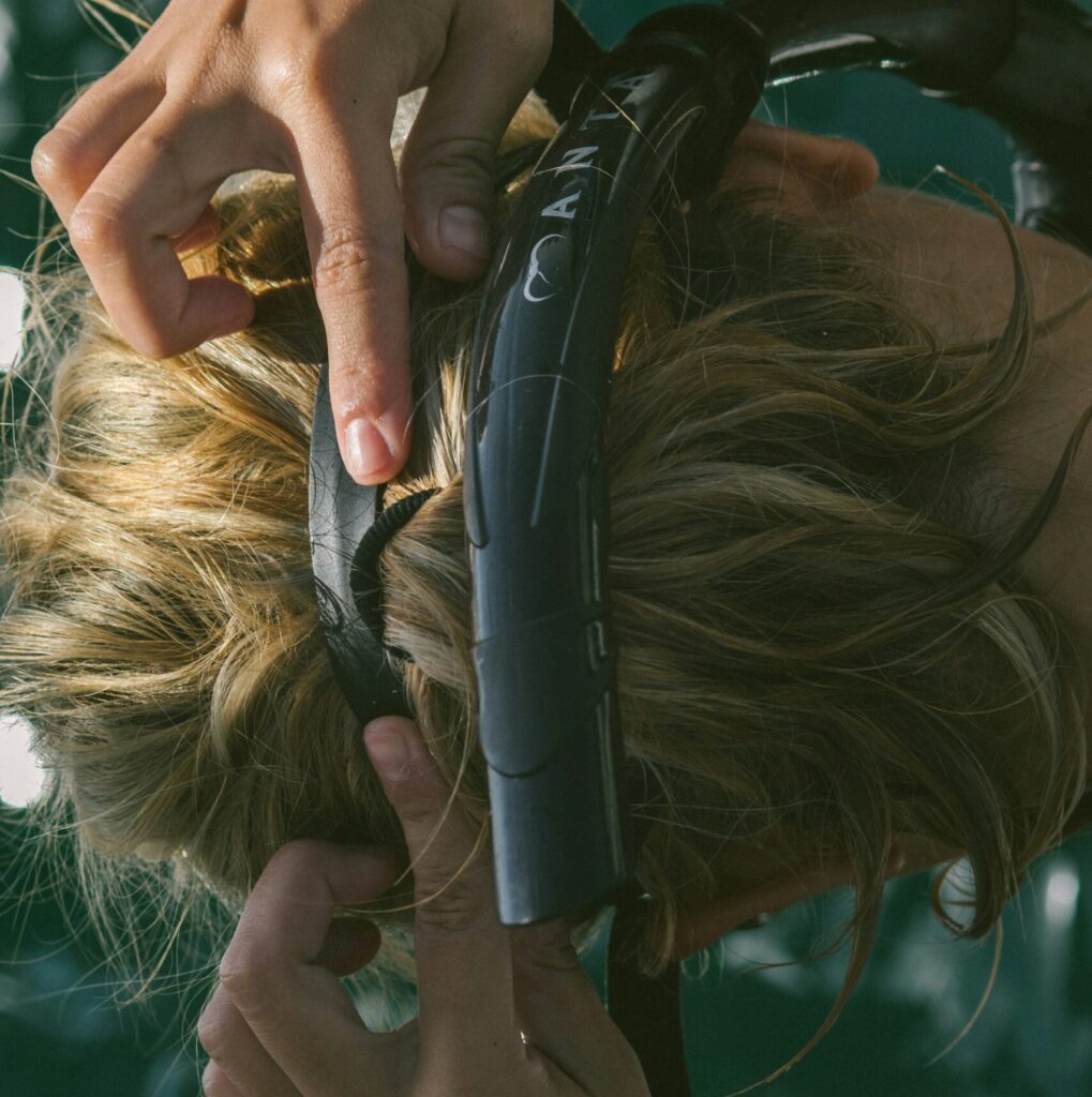 Mulher aplicando protetor térmico em spray no cabelo seco antes de usar a chapinha para fazer cachos.